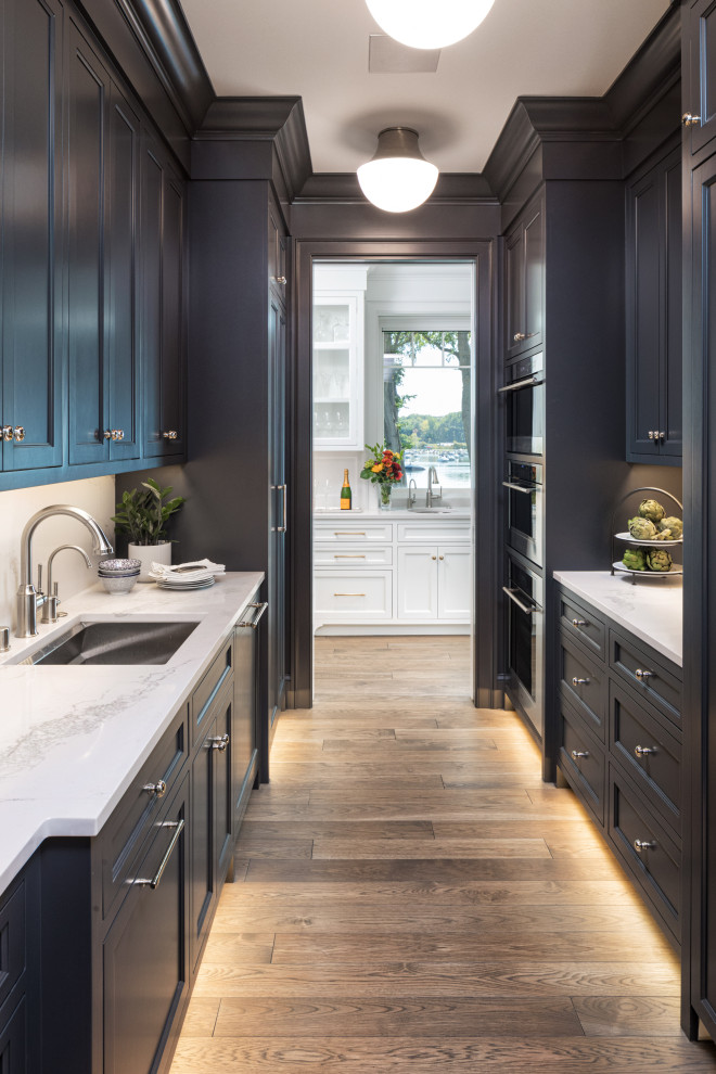 Zweizeilige Maritime Küche mit Vorratsschrank, Unterbauwaschbecken, Schrankfronten im Shaker-Stil, schwarzen Schränken, braunem Holzboden und weißer Arbeitsplatte in Minneapolis