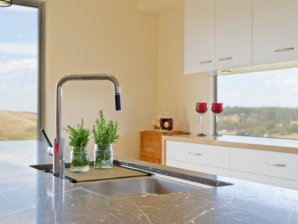 Immagine di una cucina minimalista con lavello a doppia vasca, ante bianche, top in marmo e elettrodomestici neri