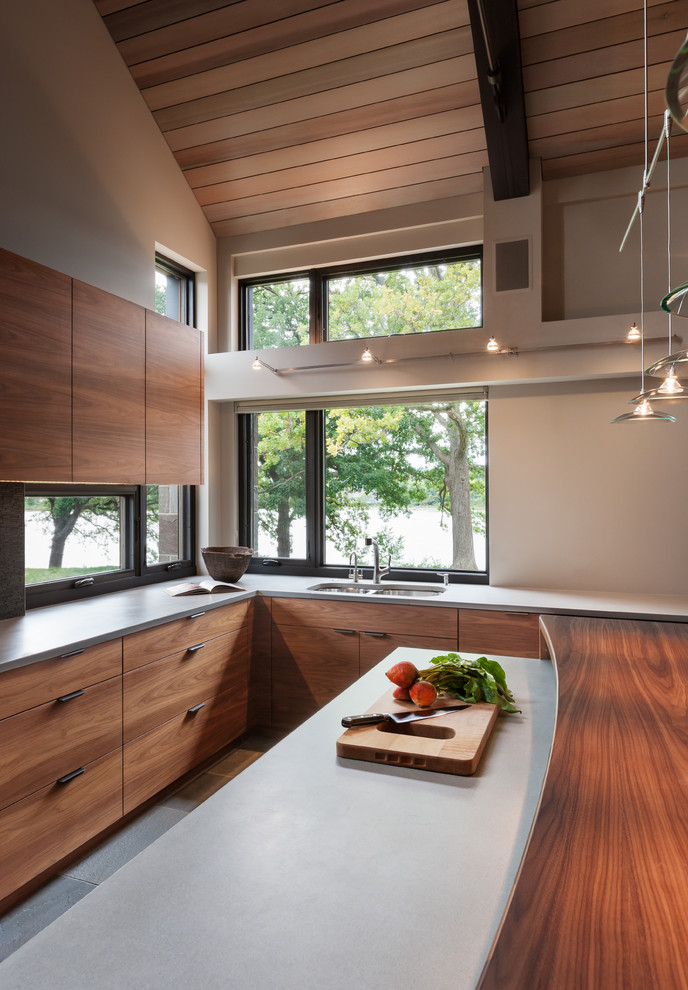 Modern inredning av ett kök, med skåp i mellenmörkt trä, bänkskiva i betong, rostfria vitvaror och en köksö