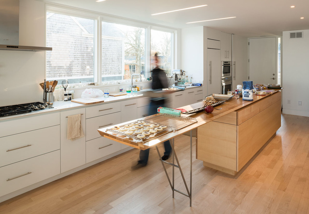 Ejemplo de cocina lineal contemporánea con armarios con paneles lisos, puertas de armario blancas, electrodomésticos con paneles y encimera de madera