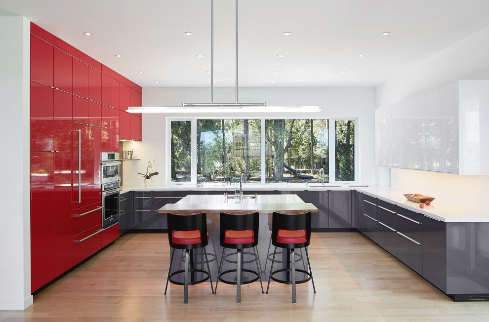 Große Moderne Küche in U-Form mit flächenbündigen Schrankfronten, roten Schränken, Küchenrückwand in Weiß, Elektrogeräten mit Frontblende, hellem Holzboden, Kücheninsel, weißer Arbeitsplatte, Unterbauwaschbecken und braunem Boden in Sonstige