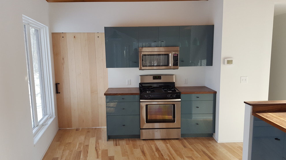 Photo of a small contemporary l-shaped kitchen/diner in New York with a built-in sink, flat-panel cabinets, turquoise cabinets, wood worktops, brown splashback, wood splashback, stainless steel appliances, light hardwood flooring and no island.