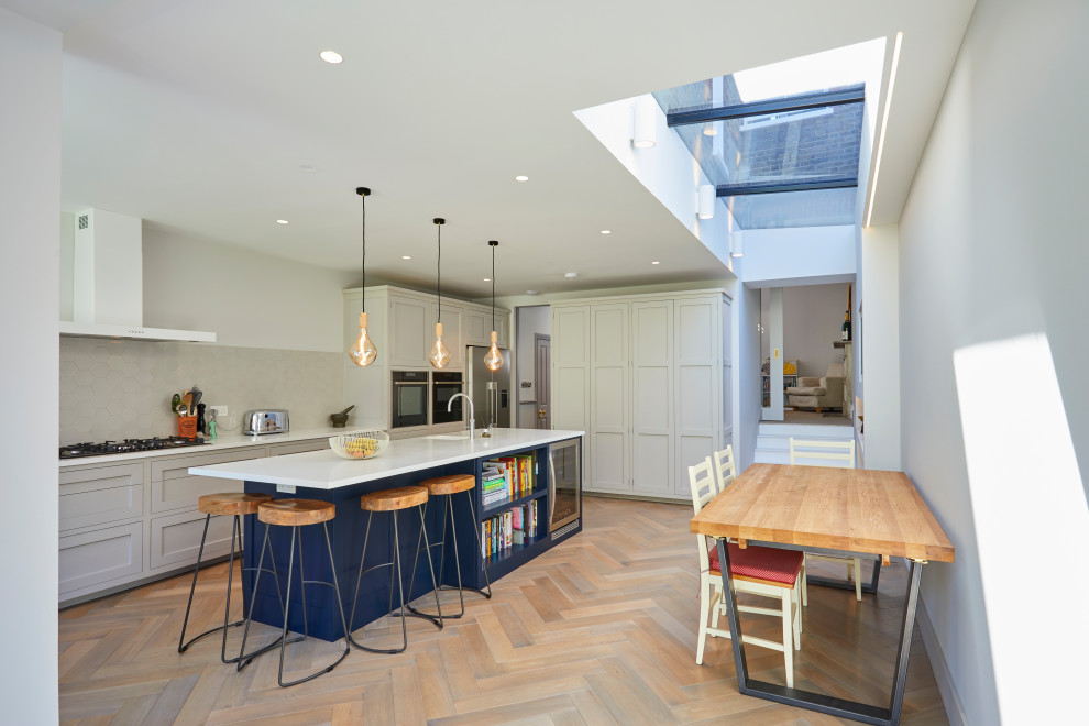 Inspiration for a contemporary galley kitchen/diner in London with a submerged sink, composite countertops, medium hardwood flooring, an island, beige floors, white worktops, shaker cabinets, grey cabinets, grey splashback and stainless steel appliances.