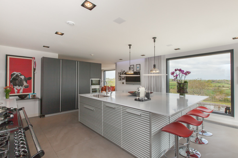 Foto på ett mellanstort industriellt l-kök, med en undermonterad diskho, släta luckor, grå skåp, en köksö och grått golv