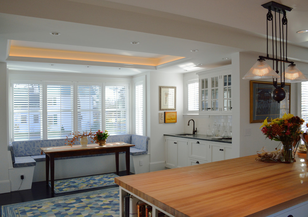 Example of a classic eat-in kitchen design in Portland Maine with shaker cabinets, wood countertops, white cabinets, an undermount sink, white backsplash and subway tile backsplash