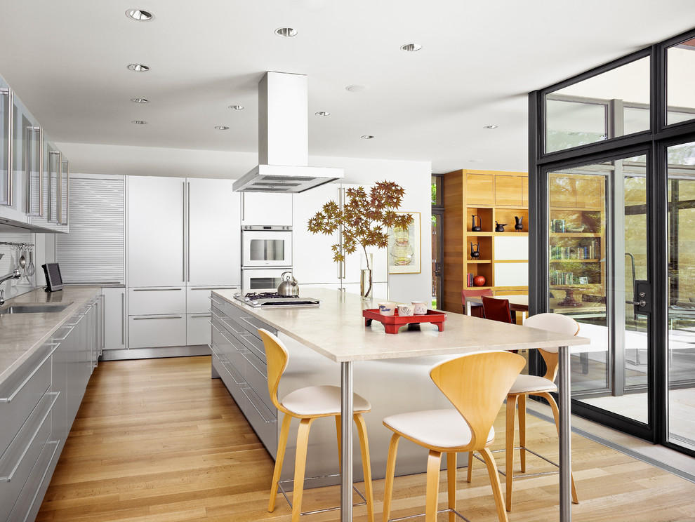 Foto di una cucina minimalista con lavello sottopiano, ante lisce, top in granito, paraspruzzi bianco, paraspruzzi con lastra di vetro e parquet chiaro