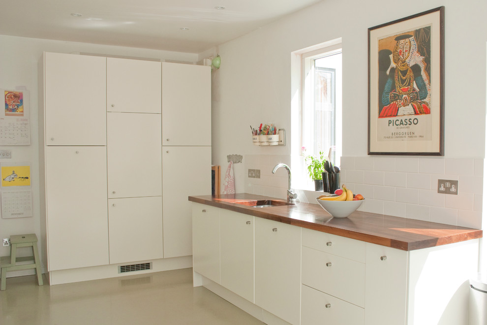Inspiration for a contemporary beige floor kitchen remodel in Other with wood countertops, flat-panel cabinets, white cabinets, an undermount sink, white backsplash and subway tile backsplash