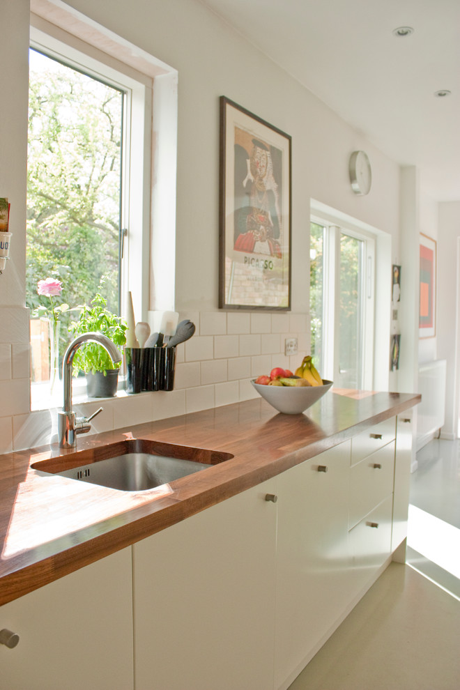 Exempel på ett modernt kök, med träbänkskiva, släta luckor, vita skåp, stänkskydd i tunnelbanekakel och vitt stänkskydd