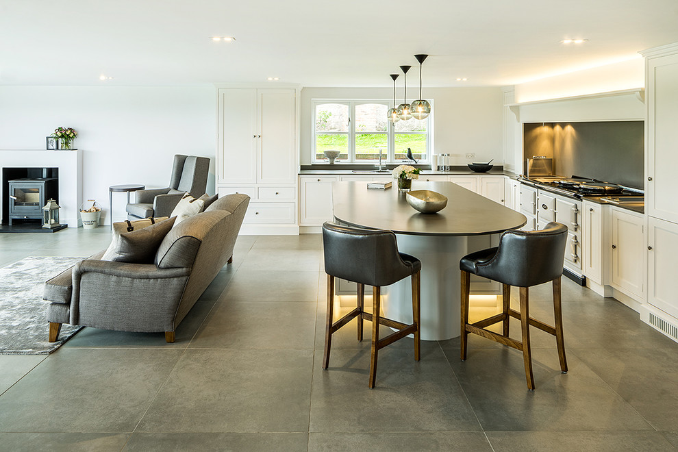 This is an example of a traditional l-shaped open plan kitchen in Other with shaker cabinets, grey splashback, concrete flooring, an island, white cabinets and white appliances.