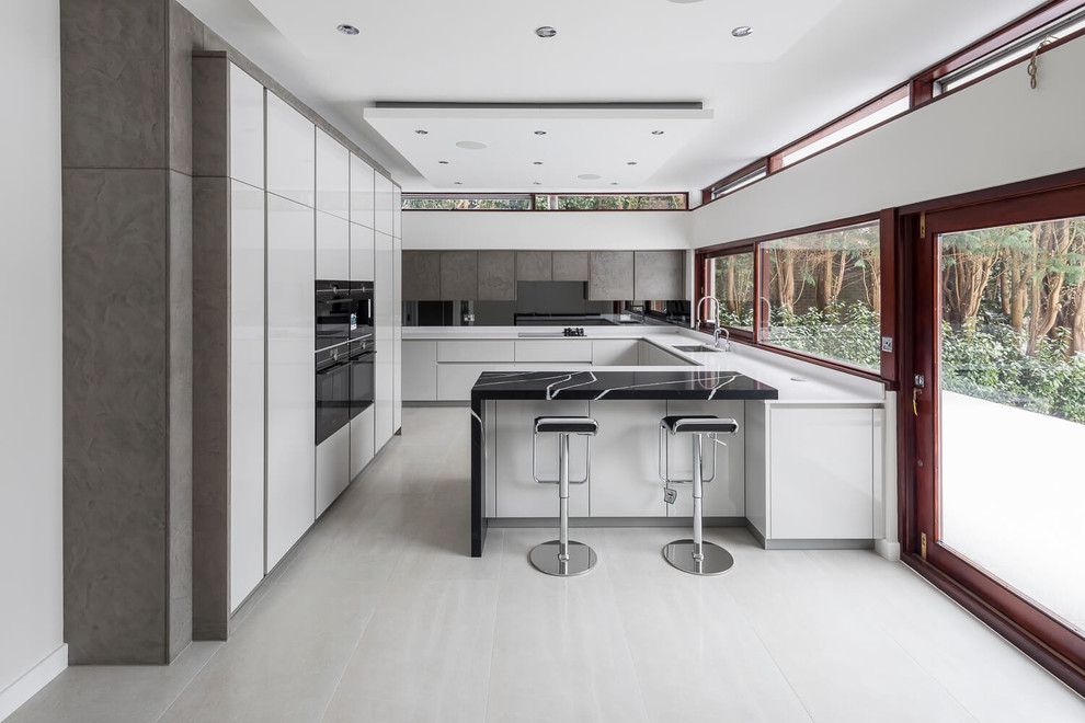 Inspiration för stora moderna vitt u-kök, med en undermonterad diskho, släta luckor, vita skåp, svart stänkskydd, svarta vitvaror, en halv köksö och grått golv