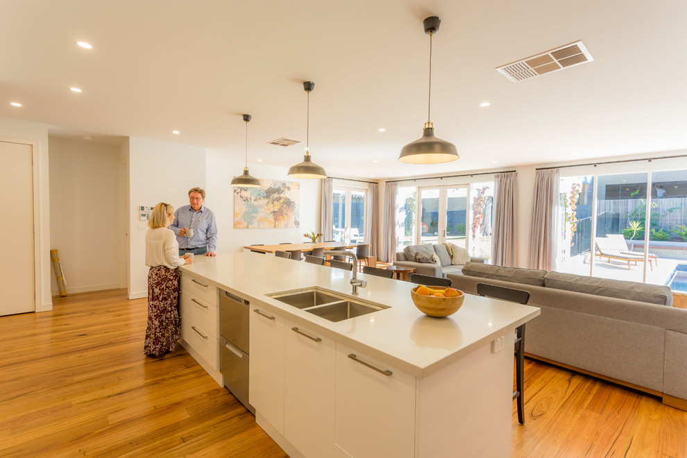 Inspiration for a medium sized contemporary galley open plan kitchen in Melbourne with a submerged sink, recessed-panel cabinets, white cabinets, engineered stone countertops, metallic splashback, ceramic splashback, stainless steel appliances, medium hardwood flooring, an island and beige worktops.