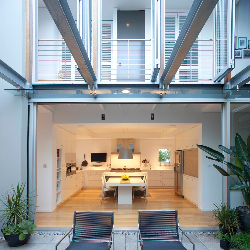 Große Moderne Wohnküche in U-Form mit flächenbündigen Schrankfronten, weißen Schränken, Küchenrückwand in Weiß, Küchengeräten aus Edelstahl, hellem Holzboden und Kücheninsel in Sydney