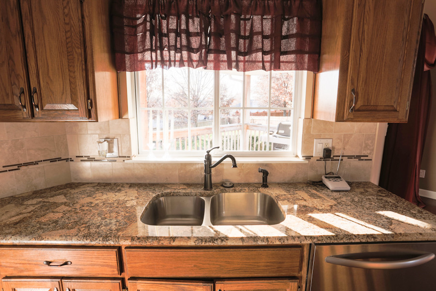 Exemple d'une cuisine américaine parallèle chic en bois brun de taille moyenne avec un évier 2 bacs, un placard avec porte à panneau surélevé, un plan de travail en granite, une crédence beige, une crédence en carreau de porcelaine, un électroménager en acier inoxydable et un sol en bois brun.