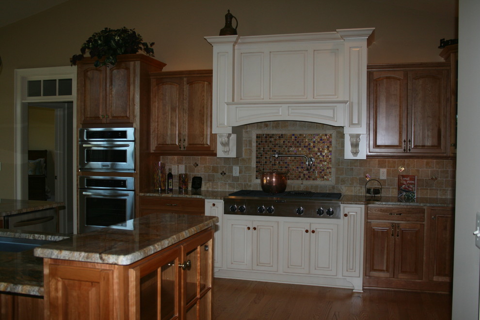 Inredning av ett klassiskt stort kök, med en undermonterad diskho, luckor med upphöjd panel, skåp i ljust trä, granitbänkskiva, beige stänkskydd, stänkskydd i keramik, rostfria vitvaror, ljust trägolv och en köksö