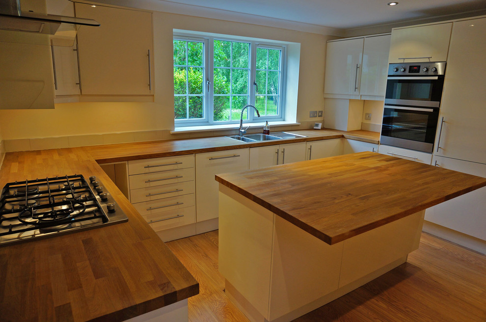 Inspiration for a traditional u-shaped open plan kitchen in Buckinghamshire with flat-panel cabinets, white cabinets, laminate countertops, beige splashback, ceramic splashback, stainless steel appliances and an island.