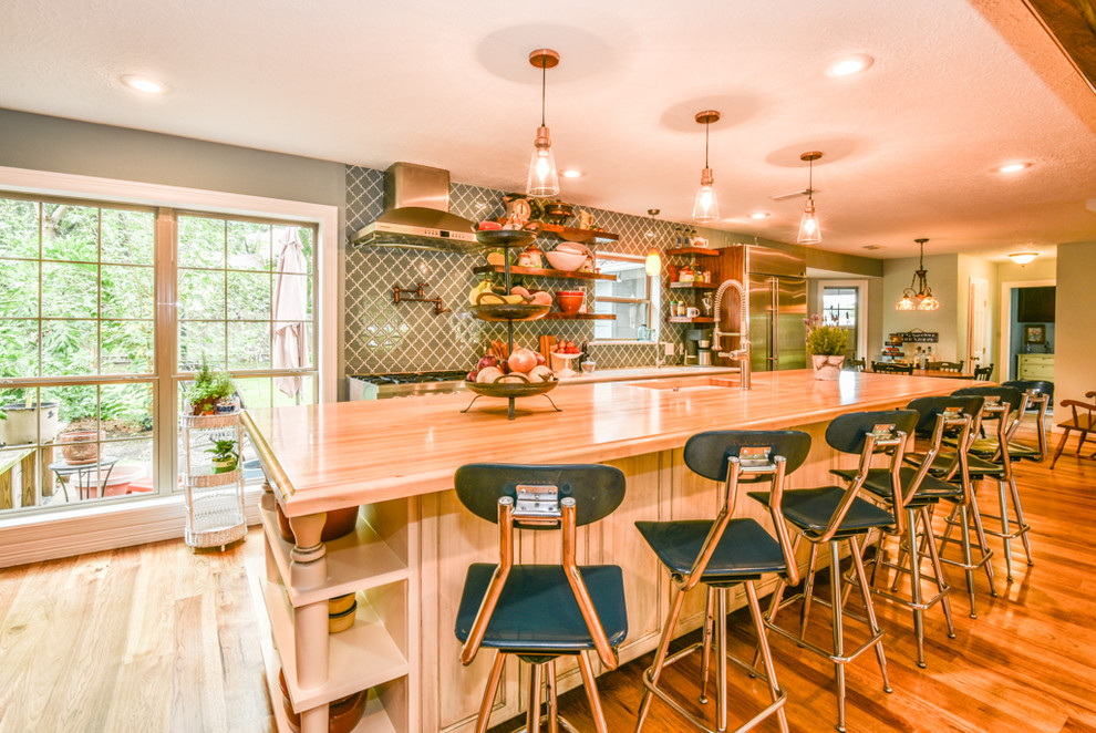 Example of a single-wall medium tone wood floor and beige floor eat-in kitchen design in Houston with a drop-in sink, recessed-panel cabinets, distressed cabinets, wood countertops, blue backsplash, glass tile backsplash, stainless steel appliances and an island