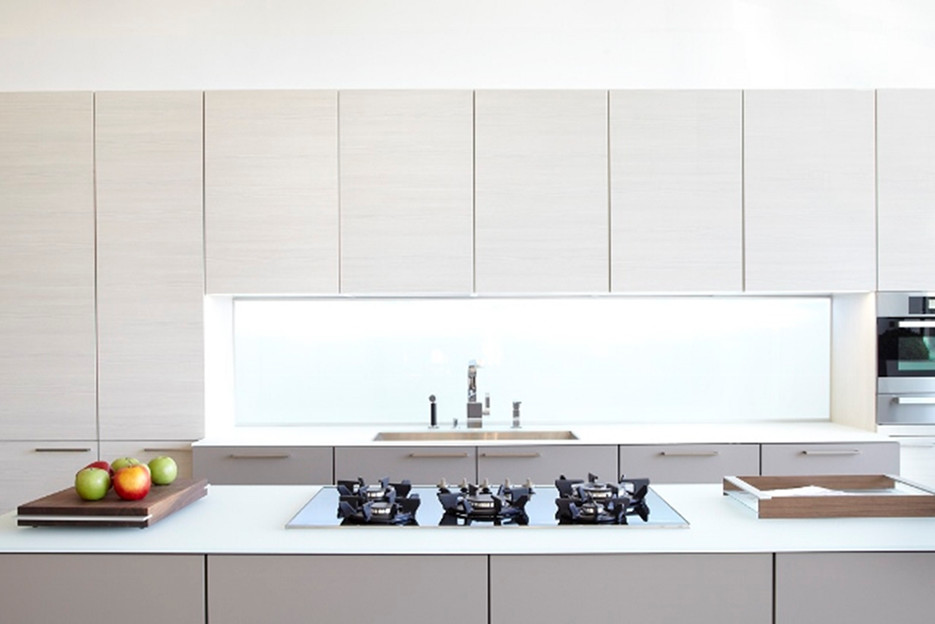 Modern inredning av ett mellanstort linjärt kök med öppen planlösning, med en undermonterad diskho, släta luckor, skåp i ljust trä, bänkskiva i glas, glaspanel som stänkskydd, svarta vitvaror, mörkt trägolv och en köksö