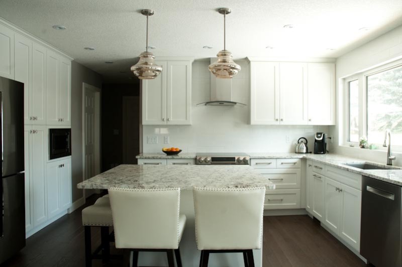 Klassisk inredning av ett kök, med vita skåp, vitt stänkskydd, rostfria vitvaror, en köksö och brunt golv