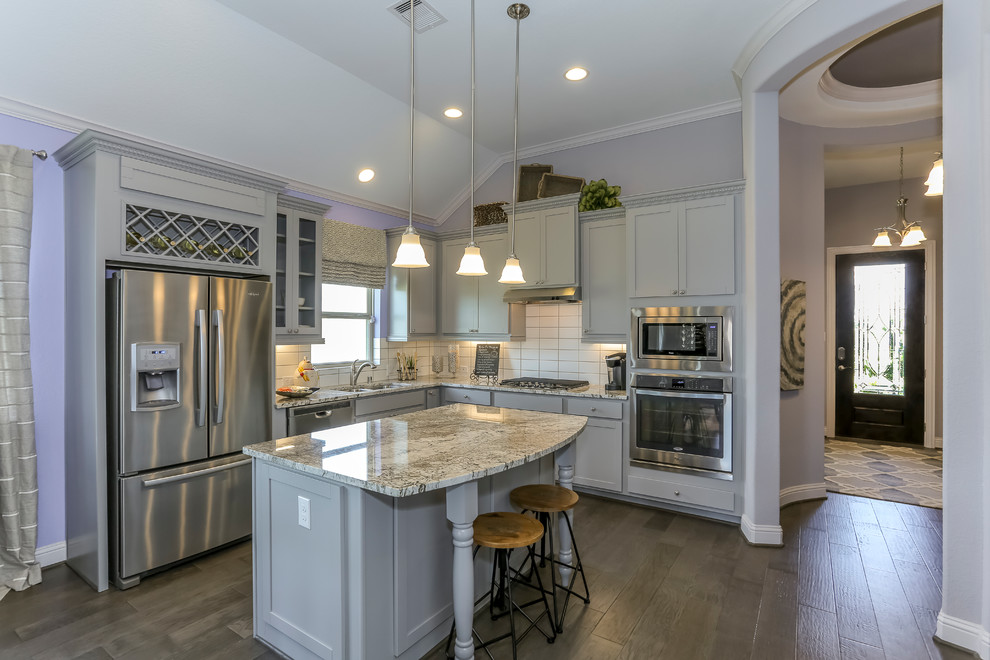 Photo of a medium sized l-shaped kitchen/diner in Houston with a double-bowl sink, recessed-panel cabinets, grey cabinets, granite worktops, white splashback, metro tiled splashback, stainless steel appliances, dark hardwood flooring, an island and purple floors.