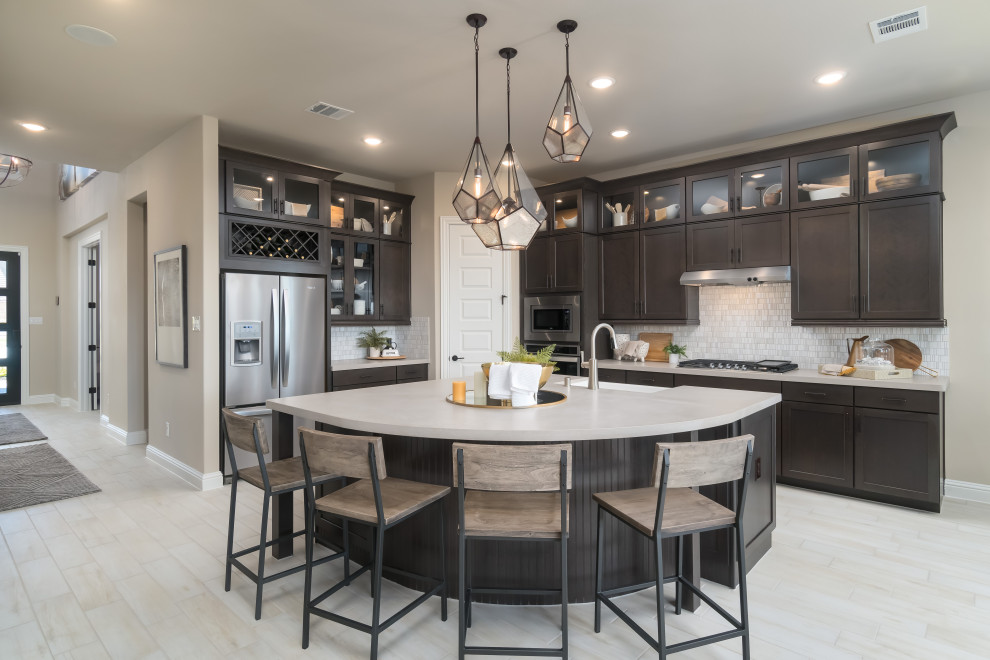 Photo of a medium sized traditional l-shaped open plan kitchen in Houston with an island, recessed-panel cabinets, composite countertops, beige splashback, ceramic splashback, stainless steel appliances, white worktops, a belfast sink, light hardwood flooring, beige floors and dark wood cabinets.