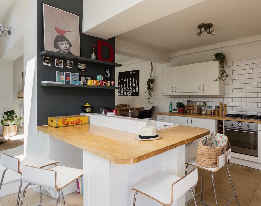 Eklektisk inredning av ett kök, med luckor med infälld panel, vita skåp, träbänkskiva, vitt stänkskydd, en köksö, brunt golv, en nedsänkt diskho och stänkskydd i tunnelbanekakel