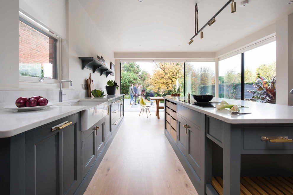 Design ideas for a medium sized traditional l-shaped open plan kitchen in Sussex with a belfast sink, beaded cabinets, blue cabinets, composite countertops, light hardwood flooring, an island and white worktops.