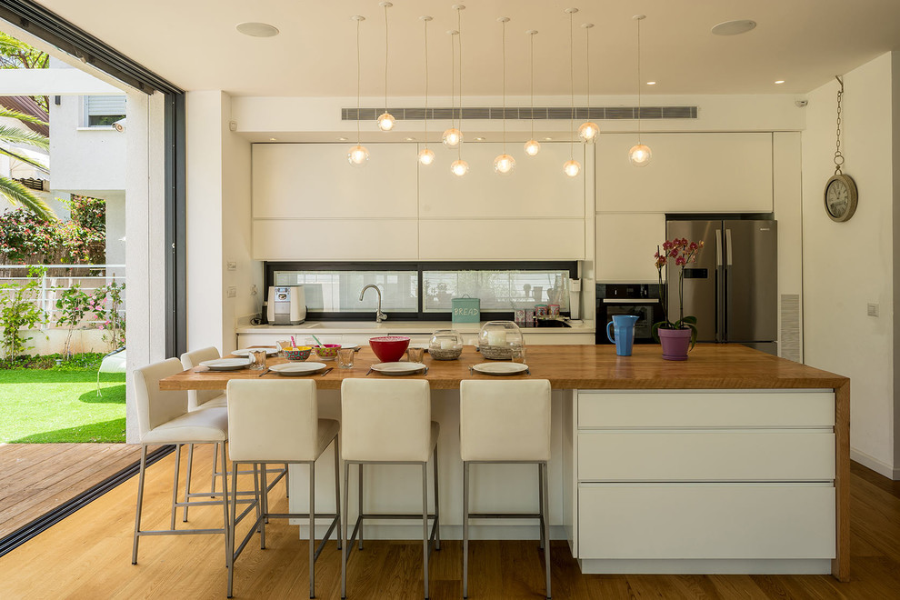 Bild på ett litet funkis kök, med släta luckor, vita skåp, träbänkskiva, rostfria vitvaror, en köksö, en enkel diskho och mellanmörkt trägolv