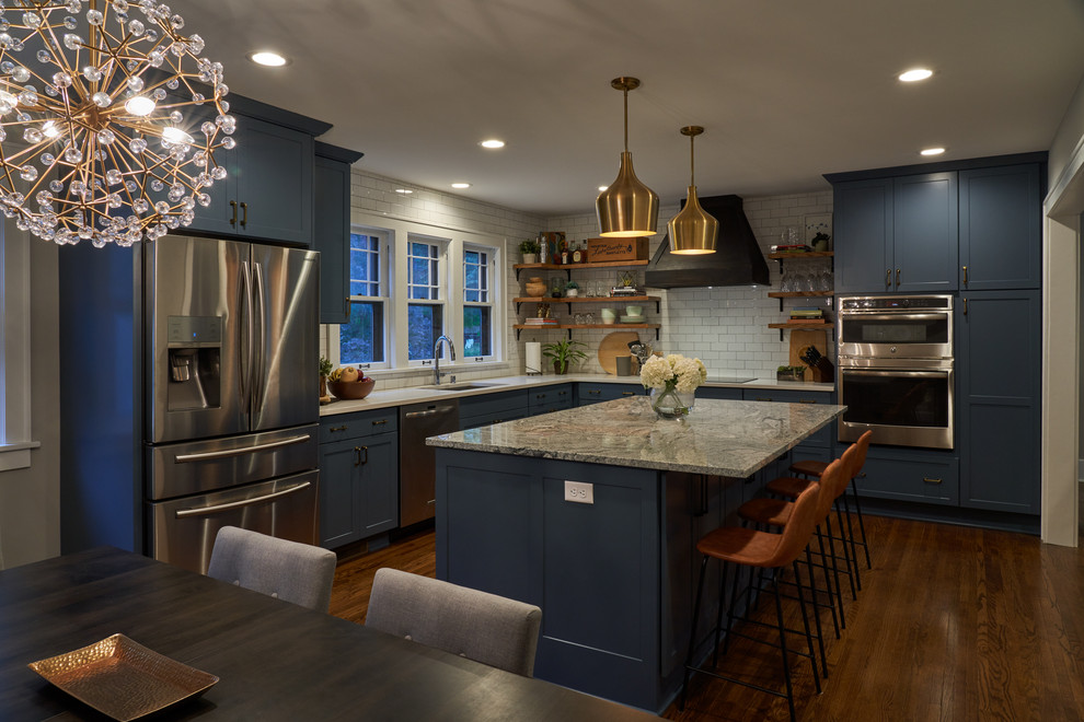 Bild på ett stort lantligt grå grått kök, med en undermonterad diskho, skåp i shakerstil, blå skåp, granitbänkskiva, vitt stänkskydd, stänkskydd i tunnelbanekakel, rostfria vitvaror, mellanmörkt trägolv, en köksö och brunt golv