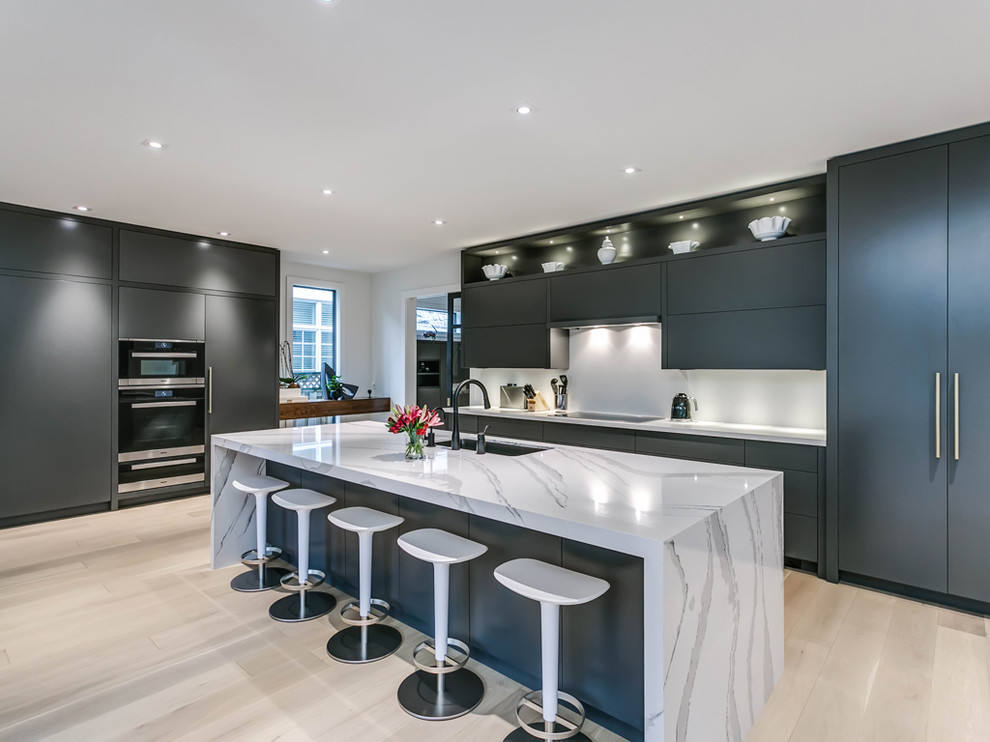 Photo of a large contemporary kitchen in Toronto with flat-panel cabinets, white splashback, integrated appliances, light hardwood flooring, an island, beige floors, white worktops, a submerged sink and blue cabinets.