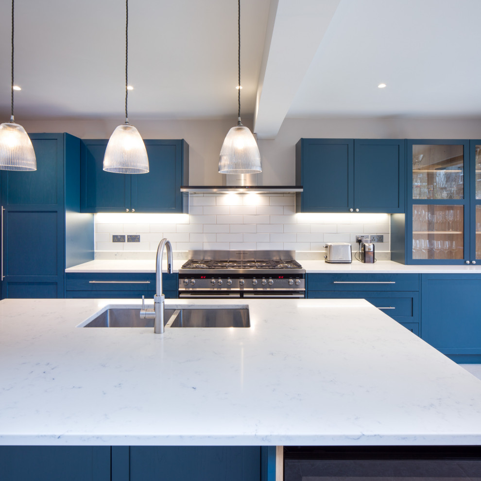 Einzeilige, Mittelgroße Moderne Wohnküche mit Doppelwaschbecken, Schrankfronten im Shaker-Stil, blauen Schränken, Granit-Arbeitsplatte, Rückwand aus Keramikfliesen, Küchengeräten aus Edelstahl, Kücheninsel und weißer Arbeitsplatte in London