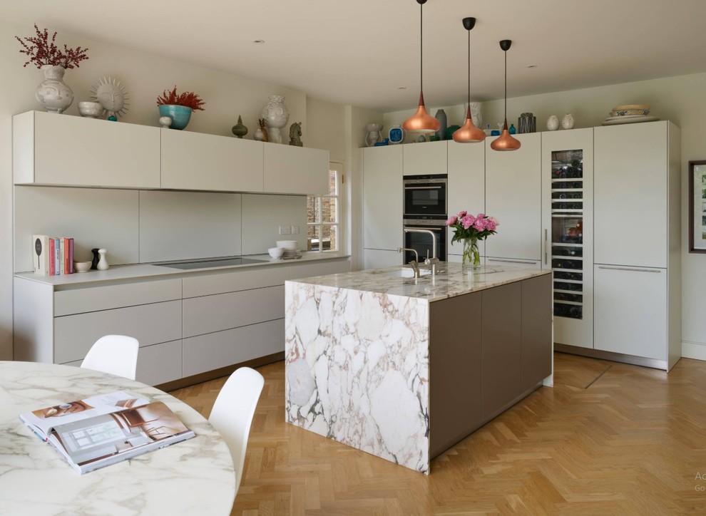 Large contemporary l-shaped kitchen/diner in London with a double-bowl sink, flat-panel cabinets, grey cabinets, composite countertops, light hardwood flooring, an island, beige floors, grey worktops and white splashback.