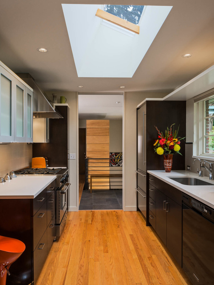 Example of a mid-sized trendy galley light wood floor kitchen design in Seattle with a single-bowl sink, flat-panel cabinets, black cabinets, stainless steel appliances, quartz countertops, gray backsplash and no island