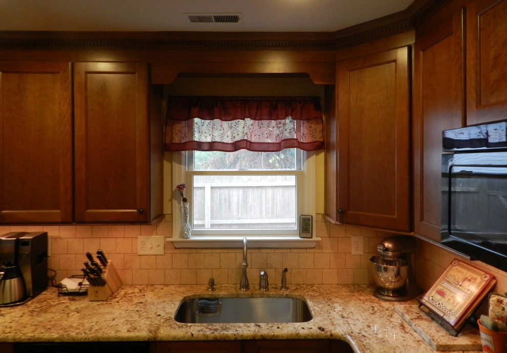 Inredning av ett klassiskt mellanstort kök, med en enkel diskho, luckor med infälld panel, skåp i mellenmörkt trä, granitbänkskiva, beige stänkskydd, stänkskydd i stenkakel, svarta vitvaror, klinkergolv i porslin och en halv köksö