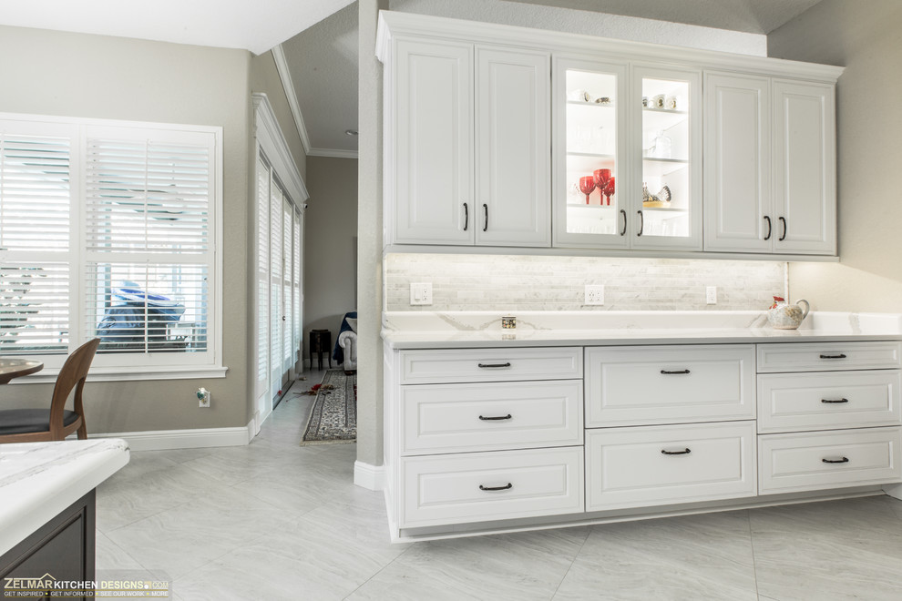 Example of a mid-sized transitional u-shaped porcelain tile and gray floor eat-in kitchen design in Orlando with an undermount sink, raised-panel cabinets, white cabinets, quartz countertops, gray backsplash, marble backsplash and an island
