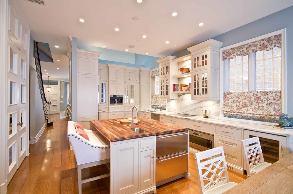 Klassisk inredning av ett stort kök, med en undermonterad diskho, luckor med profilerade fronter, vita skåp, flerfärgad stänkskydd, rostfria vitvaror, mellanmörkt trägolv och en köksö