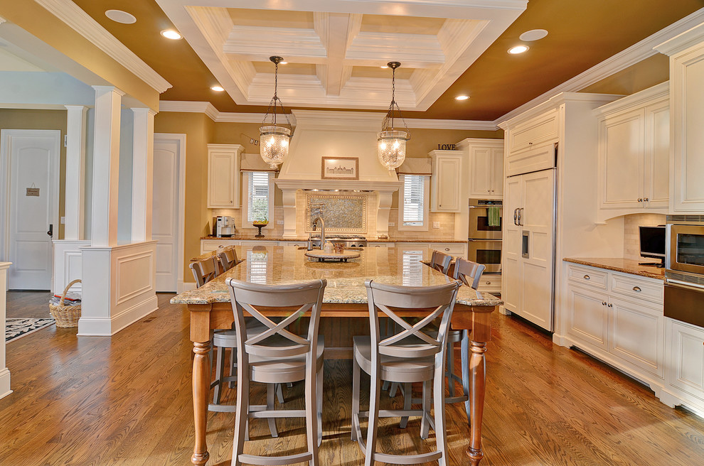 Exempel på ett stort klassiskt kök, med vita skåp, en köksö, en undermonterad diskho, luckor med infälld panel, granitbänkskiva, beige stänkskydd, stänkskydd i stenkakel, integrerade vitvaror, mellanmörkt trägolv och brunt golv