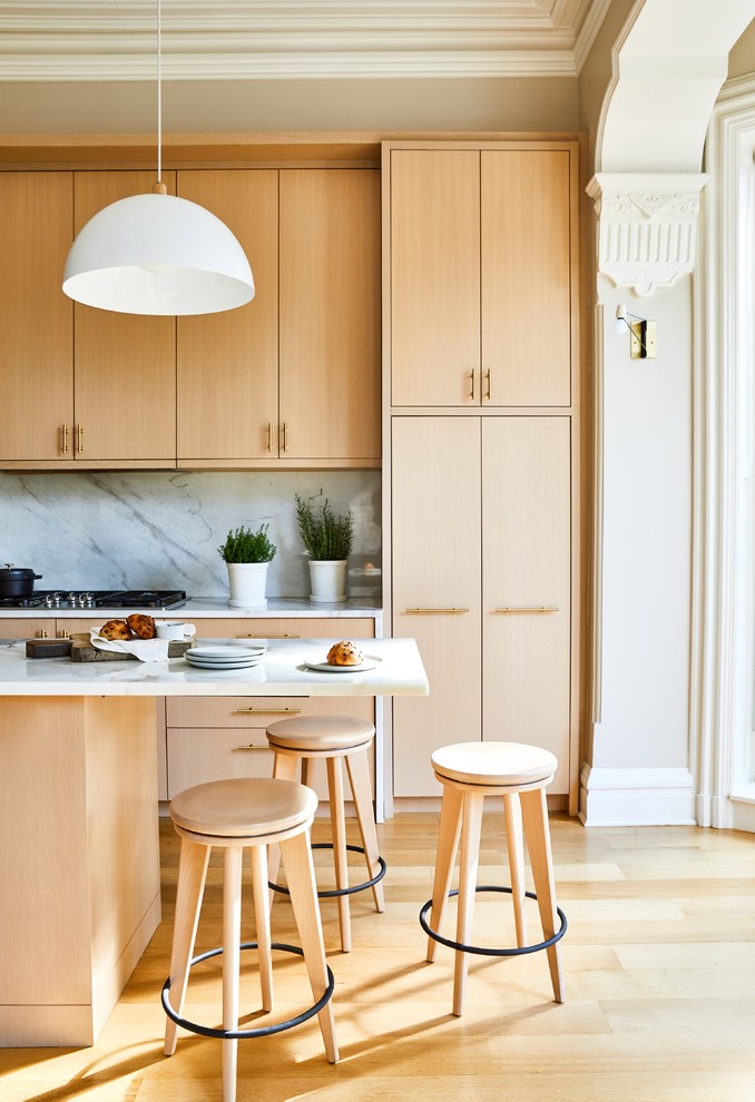 Example of a transitional light wood floor and beige floor kitchen design in New York with flat-panel cabinets, light wood cabinets, white backsplash, stone slab backsplash, an island and white countertops