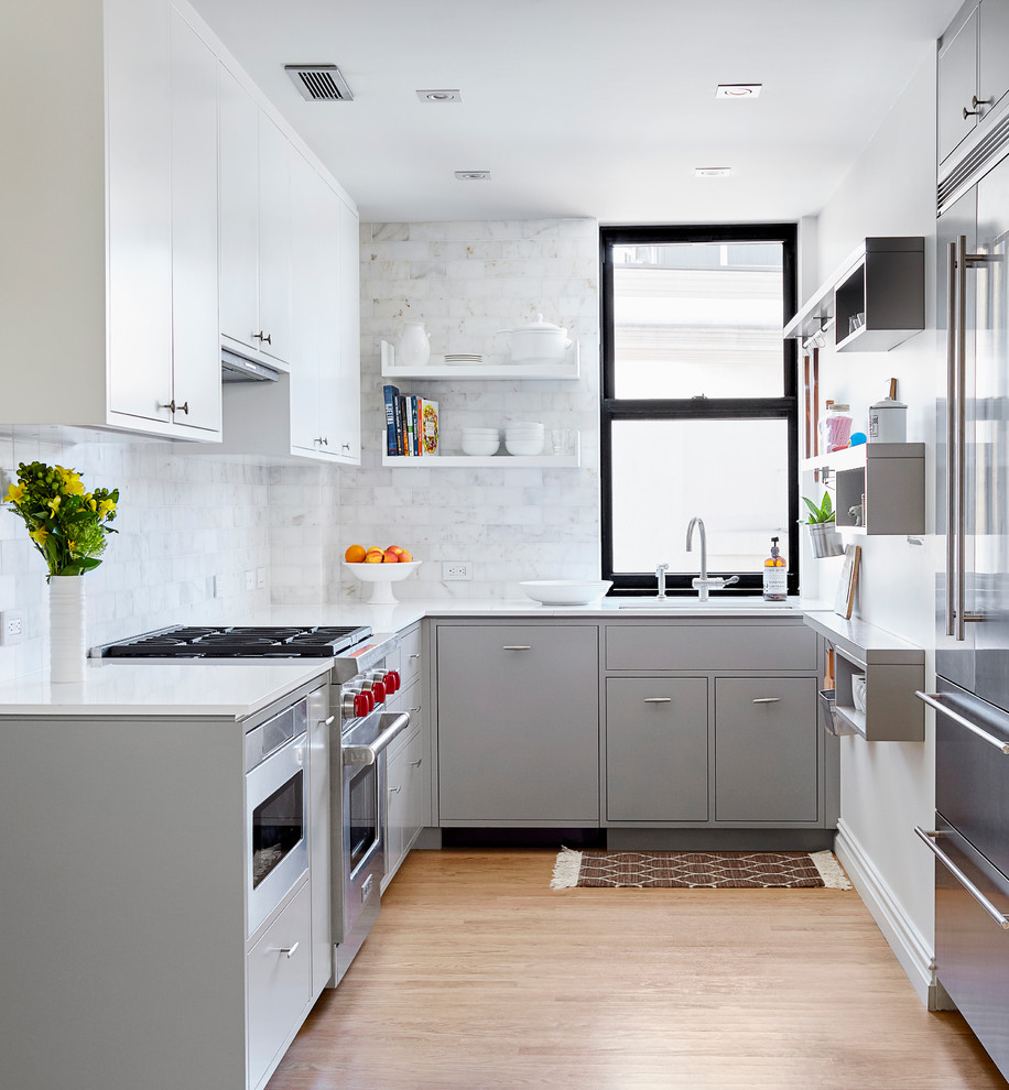 Inspiration for a small contemporary grey and white u-shaped open plan kitchen in New York with a submerged sink, flat-panel cabinets, grey cabinets, engineered stone countertops, white splashback, stone tiled splashback, stainless steel appliances, no island and light hardwood flooring.