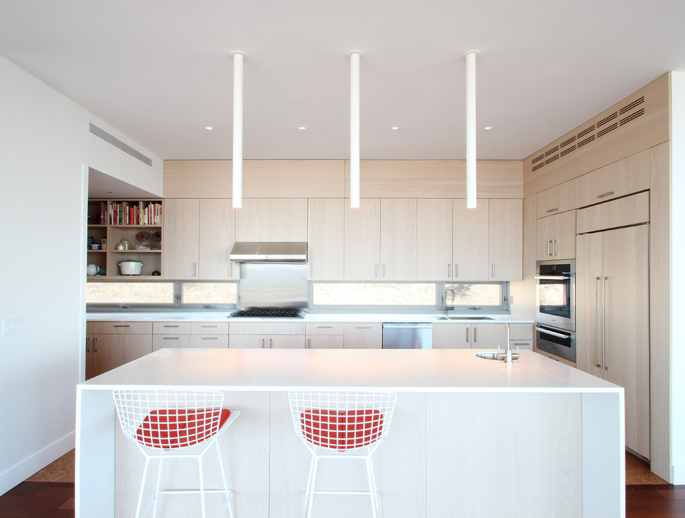 Modern kitchen in New York with a submerged sink, flat-panel cabinets, light wood cabinets, stainless steel appliances and an island.