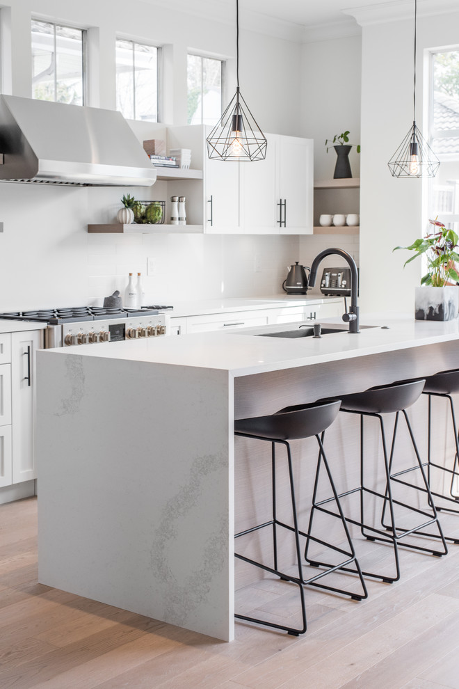 Kitchen - scandinavian l-shaped light wood floor kitchen idea in Vancouver with an undermount sink, shaker cabinets, white cabinets, quartz countertops, white backsplash, stainless steel appliances, an island and white countertops