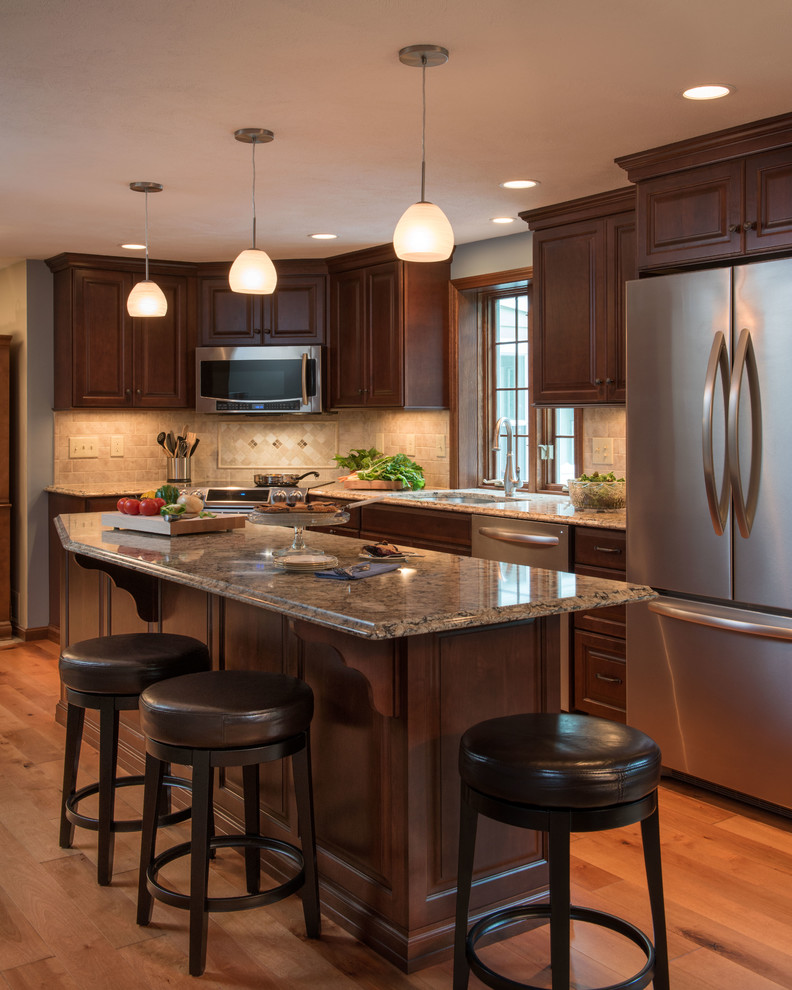 Example of a large transitional single-wall medium tone wood floor eat-in kitchen design in Manchester with a double-bowl sink, dark wood cabinets, granite countertops, beige backsplash, ceramic backsplash, stainless steel appliances and an island