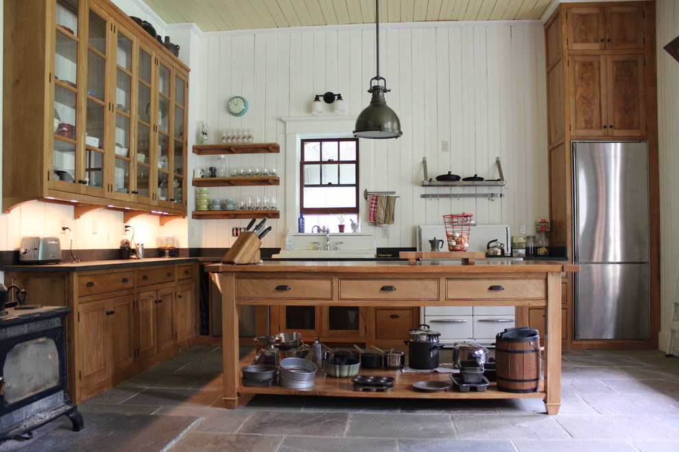 Bild på ett stort lantligt kök, med en dubbel diskho, luckor med profilerade fronter, skåp i mellenmörkt trä, bänkskiva i täljsten, svart stänkskydd, skiffergolv och en köksö