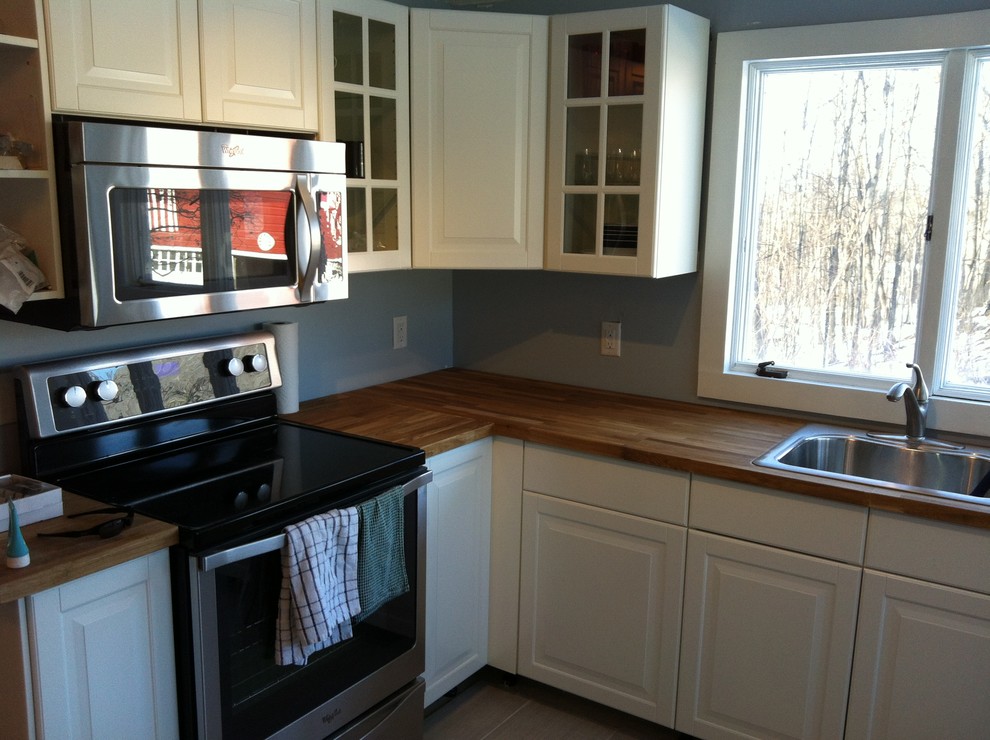 Example of a mid-sized cottage galley porcelain tile enclosed kitchen design in New York with a single-bowl sink, raised-panel cabinets, white cabinets, wood countertops, blue backsplash, stainless steel appliances and no island