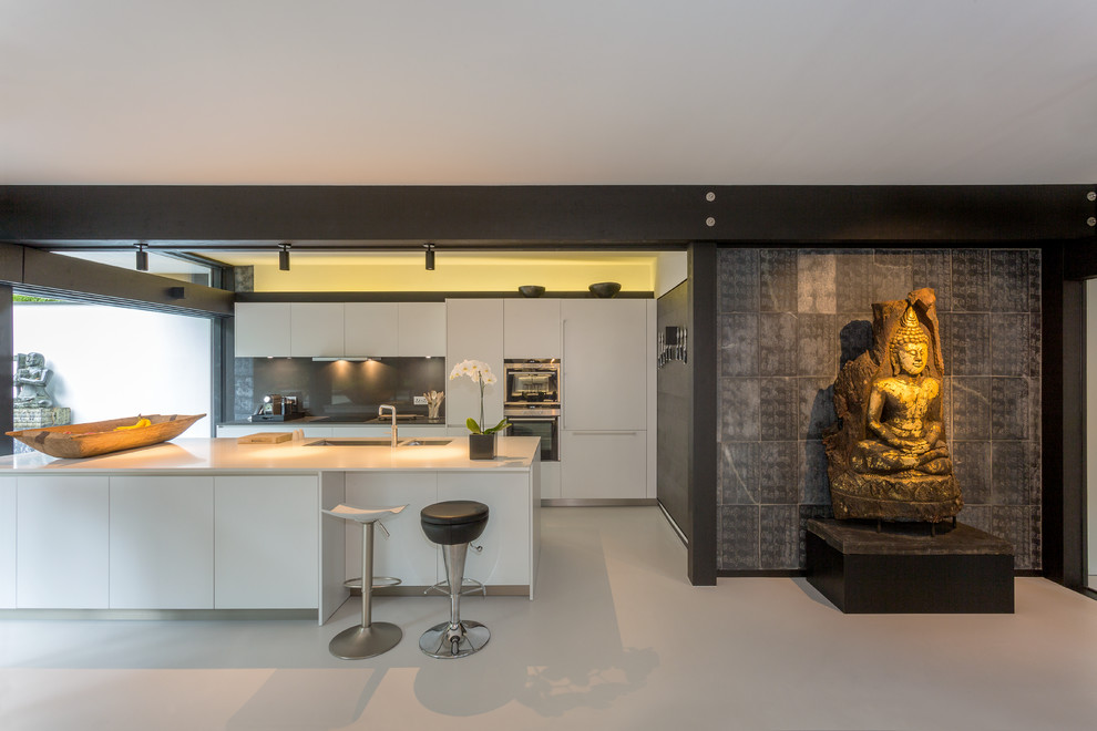 ロンドンにあるアジアンスタイルのおしゃれなアイランドキッチン (ダブルシンク、フラットパネル扉のキャビネット、白いキャビネット、グレーのキッチンパネル、シルバーの調理設備、グレーの床) の写真