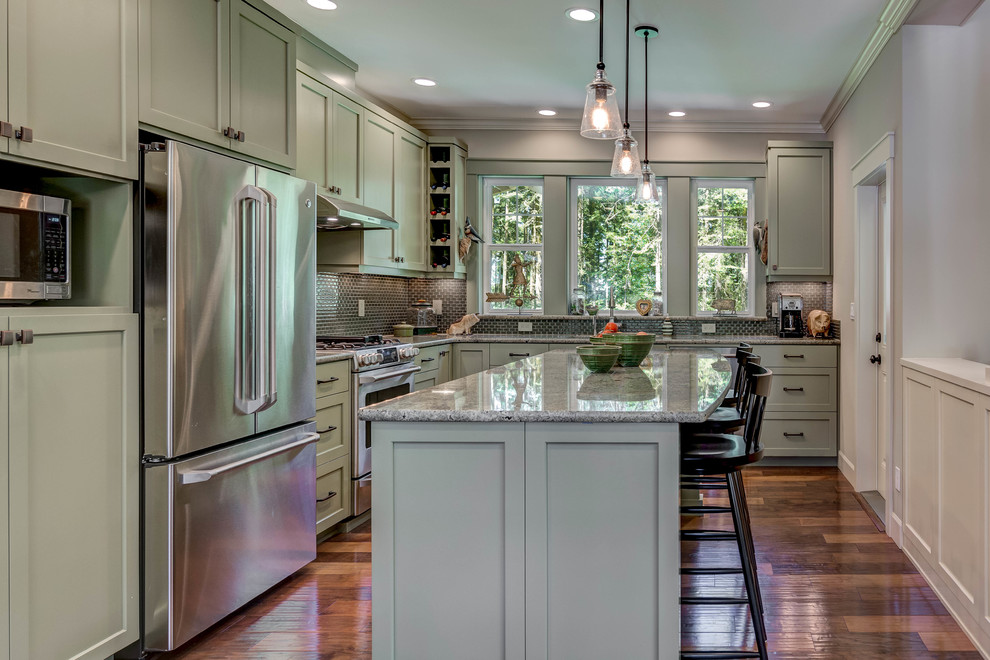 Inspiration for a mid-sized transitional l-shaped medium tone wood floor and brown floor enclosed kitchen remodel in Seattle with a double-bowl sink, shaker cabinets, green cabinets, granite countertops, green backsplash, stone tile backsplash, stainless steel appliances and an island