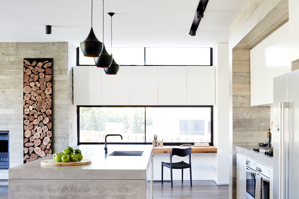 Идея дизайна: параллельная кухня-гостиная в стиле модернизм с врезной мойкой, столешницей из бетона, техникой из нержавеющей стали, плоскими фасадами, белыми фасадами, темным паркетным полом, островом и коричневым полом