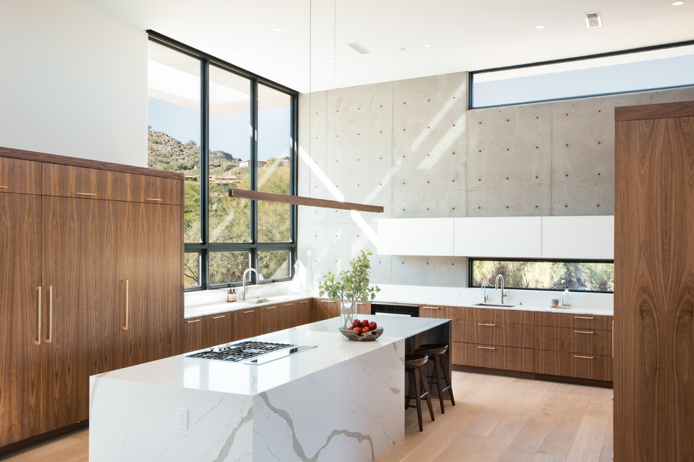 Bild på ett stort funkis vit vitt kök, med en undermonterad diskho, släta luckor, skåp i mörkt trä, bänkskiva i kvarts, vitt stänkskydd, stänkskydd i sten, integrerade vitvaror, ljust trägolv och en köksö