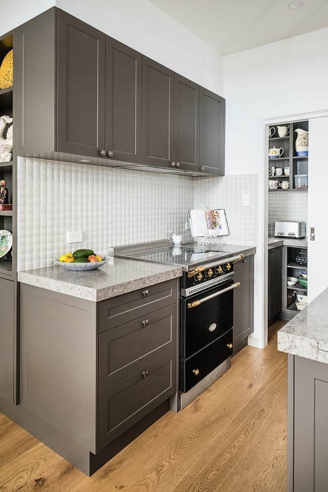 Small transitional l-shaped medium tone wood floor kitchen pantry photo in Melbourne with an undermount sink, shaker cabinets, gray cabinets, quartz countertops, white backsplash, ceramic backsplash, black appliances, an island and gray countertops