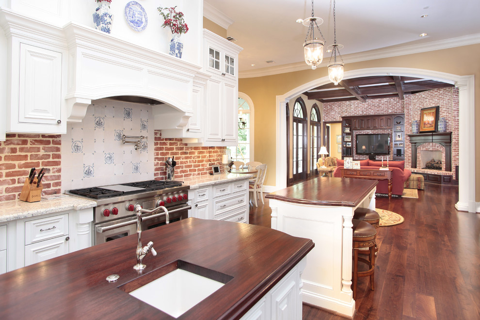 Bild på ett avskilt, mellanstort lantligt linjärt kök, med en undermonterad diskho, luckor med profilerade fronter, vita skåp, träbänkskiva, rött stänkskydd, stänkskydd i tegel, rostfria vitvaror, mellanmörkt trägolv, flera köksöar och brunt golv