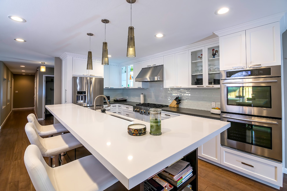 Large trendy u-shaped medium tone wood floor and brown floor eat-in kitchen photo in San Francisco with an undermount sink, shaker cabinets, white cabinets, quartz countertops, stainless steel appliances, an island, gray backsplash, glass tile backsplash and white countertops